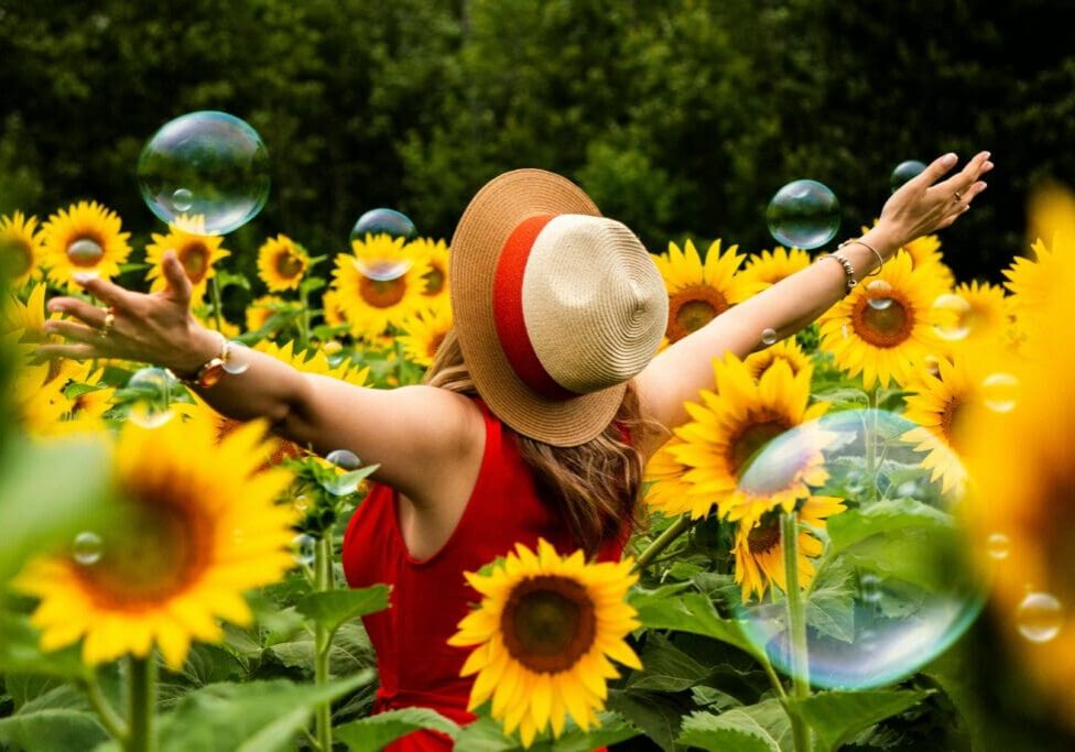 A woman in red dress and straw hat standing among sunflowers.